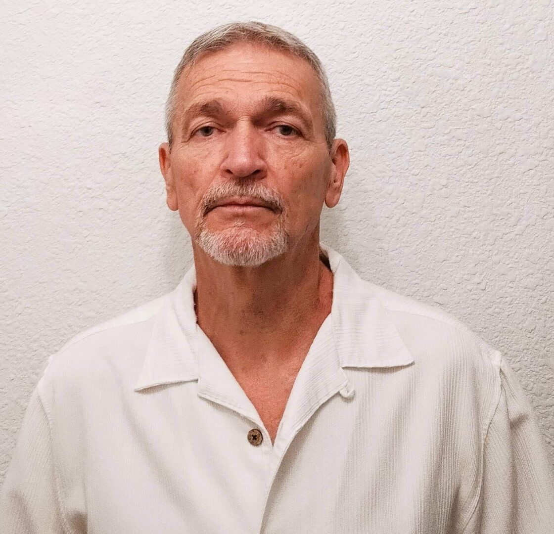 Portrait of a mature man in a white shirt against a plain background.