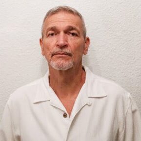 Portrait of a mature man in a white shirt against a plain background.
