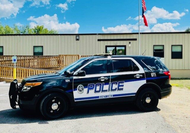 Black and white police SUV parked outside a building under a blue sky.